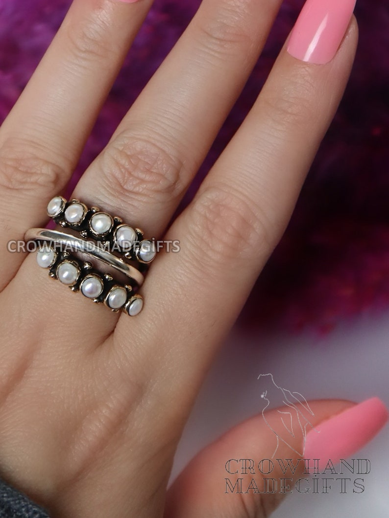 May include: A silver ring with a double row of white pearls. The ring is on a finger with pink nail polish.