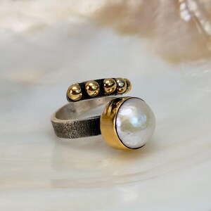 May include: A silver and gold ring with a white pearl and a row of gold beads.