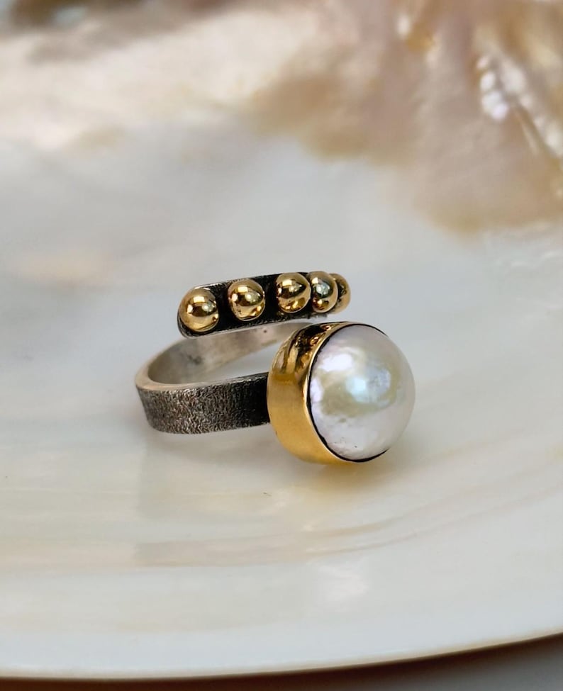 May include: A silver and gold ring with a white pearl and a row of gold beads.