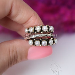 May include: Two silver rings with a row of white pearls on each. The rings are stacked on top of each other. The rings are on a finger.