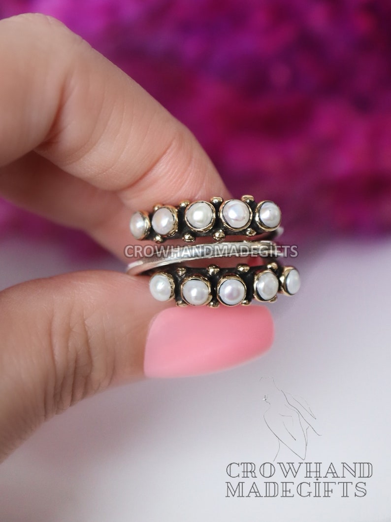 May include: Two silver rings with a row of white pearls on each. The rings are stacked on top of each other. The rings are on a finger.