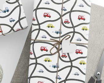 May include: Three wrapped gifts with white paper featuring a road and car pattern in red, yellow, blue, and gray. The gifts are tied with twine and have blank tags. A ball of twine, scissors, and blank tags are also visible.