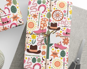 May include: Three wrapped gifts with a white background. The wrapping paper features a repeating pattern of cowboy hats, boots, cacti, and sheriff badges in pink, brown, and orange. The gifts are tied with twine and have white heart-shaped tags.