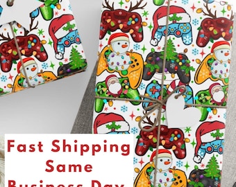 May include: White wrapping paper with a repeating pattern of colorful video game controllers, Christmas trees, snowmen, and Santa Claus wearing Santa hats. The controllers are decorated with Christmas lights. The text "Fast Shipping Same Business Day (U.S. Only)" is printed on the bottom of the image.
