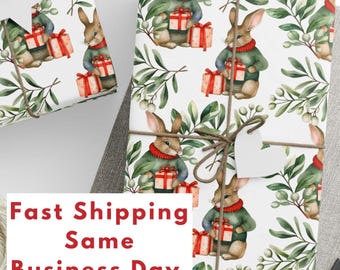 May include: White wrapping paper with a repeating pattern of brown rabbits holding red and white gift boxes. The rabbits are wearing green sweaters with white trim. Green leafy branches with white berries are scattered throughout the pattern. The text "Fast Shipping Same Business Day (U.S. Only)" is printed in red at the bottom of the image.
