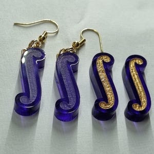 May include: A pair of earrings with a purple and gold design. The earrings are shaped like a musical note.