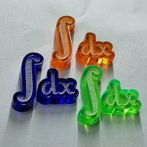 Puede incluir: Cuatro símbolos de integral de plástico con el texto "dx" en blanco. Los símbolos son de color naranja, azul, verde y transparente.