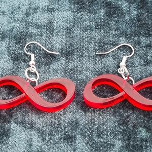 May include: A pair of red infinity symbol earrings with silver hooks. The earrings are made of acrylic and have a glossy finish.