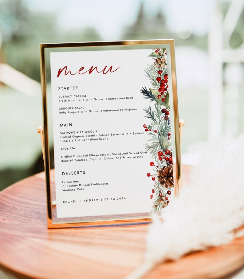 May include: A rectangular menu card in a gold metal frame featuring the word menu in red script, followed by a list of food items including Buffalo Caprese, Arugula Salad, Salmone Alla Griglia, Tagliata, and desserts, with a pine and berry border.