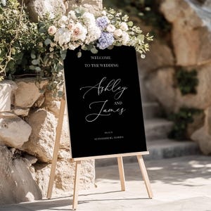 Könnte beinhalten: Schwarzes Hochzeitsschild mit weißem Text. Das Schild lautet "Willkommen zur Hochzeit von Ashley und James 08.13.23 St. Petersburg, Florida".