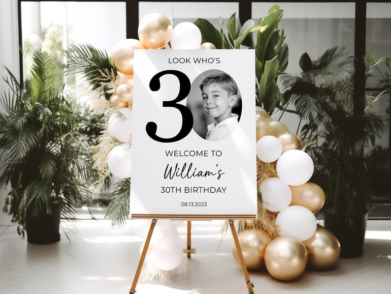 May include: A white sign with black text and a photo of a young boy. The sign reads "Look Who's 30, Welcome to William's 30th Birthday, 08.13.2023".