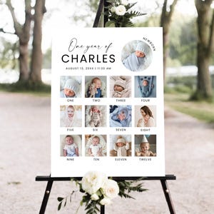May include: A white sign on a black easel displays a "One year of CHARLES" photo collage. The sign includes a newborn photo and photos for each month, numbered one through twelve. The date and time are also displayed.