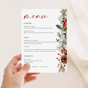 May include: A white rectangular menu card featuring the red script word menu at the top. The text lists starters, mains, and desserts with a vertical botanical border on the right side consisting of green pine needles, red berries, and a brown pinecone.