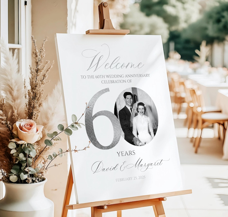 May include: A white rectangular sign on a wooden easel featuring the text Welcome to the 60th wedding anniversary celebration of, a large silver number 60, a circular black and white wedding photo, the names David & Margaret, and February 25, 2025.