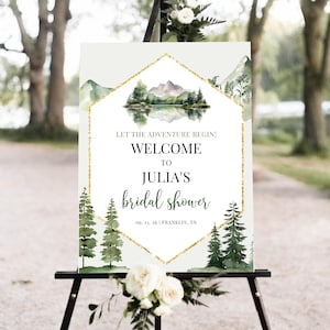 May include: A welcome sign for Julia's bridal shower, featuring a watercolor landscape with mountains, trees, and a lake. The sign includes the text "Let the adventure begin!" and the date 09.13.26, Franklin, TN.