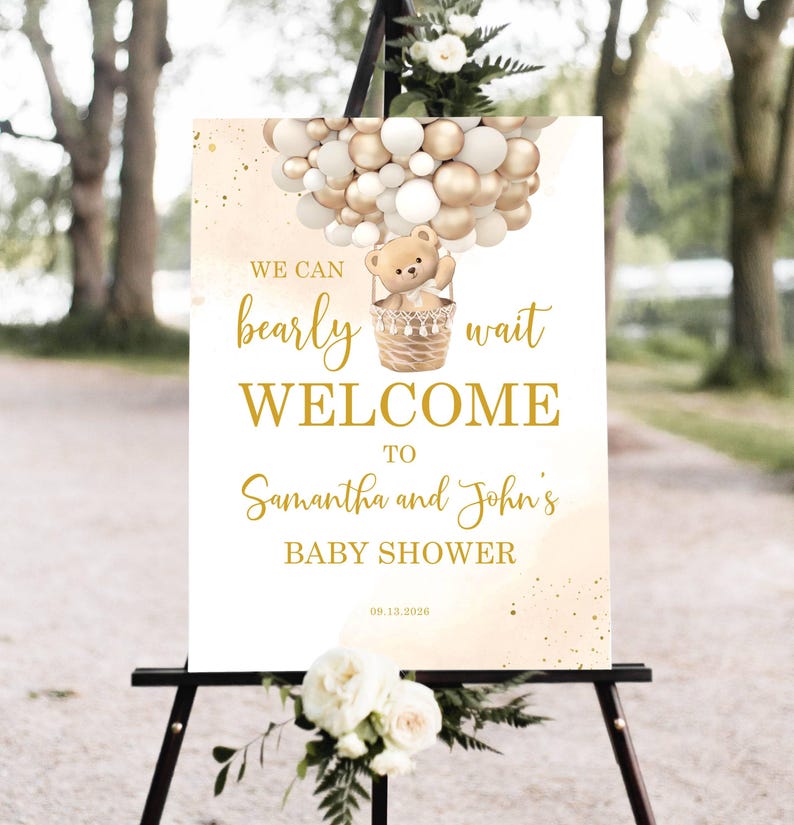 May include: A baby shower welcome sign on an easel. The sign features a teddy bear in a hot air balloon made of gold and white balloons. Text reads "We can bearly wait WELCOME to Samantha and John's BABY SHOWER" with the date 09.13.2026.