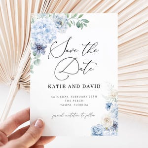 Puede incluir: Una tarjeta blanca con el texto "Save the Date" en escritura elegante, con los nombres "Katie y David". Acentos florales en tonos azules y verdes adornan las esquinas. La tarjeta incluye la fecha, el lugar y una invitación formal.