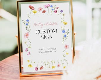 May include: A gold-framed sign with a white background, featuring the words "CUSTOM SIGN" in a stylish font. The sign is adorned with a floral border of pink, yellow, and blue flowers. The text "fully editable" and "DESIGN AND PRINT UNLIMITED SIGNS" are also visible.