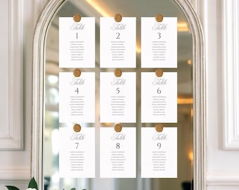May include: An arched mirror displays nine white rectangular table seating cards arranged in three rows. Each card features the word Table followed by a number from 1 to 9, a list of names, and is secured to the glass with a gold wax seal.