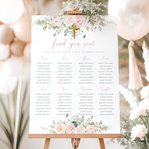May include: A white sign on an easel with a floral design and gold cross. The sign reads "find you seat" and lists names under the headings "One" through "Eight". The sign is for Rachel's First Holy Communion.