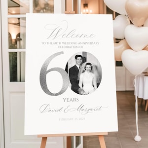 以下が含まれることがあります： 結婚60周年記念のお祝い用の白い長方形のウェルカムボード。ボードには「Welcome to the 60th wedding anniversary celebration of」という文字、大きな銀色の数字の60、カップルの円形の白黒写真、そしてDavid & Margaretという名前と2025年2月25日という日付が記載されています。
