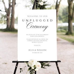 Può includere: Un cartello bianco su un cavalletto nero con il testo "WELCOME TO OUR UNPLUGGED Ceremony." Il cartello include anche il testo "WE INVITE YOU TO BE FULLY PRESENT DURING OUR CEREMONY." e "JULIA & WILLIAM 18 FEBRUARY 2026."