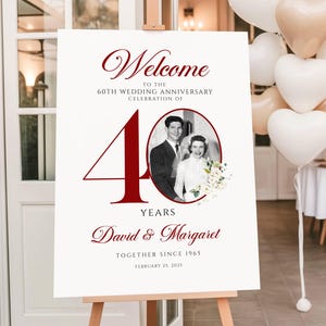 May include: A white rectangular welcome sign for a 60th wedding anniversary celebration. It features the large red number 40, a black and white oval photo of a couple, and red text reading Welcome, David & Margaret, Together Since 1965, February 25, 2025.