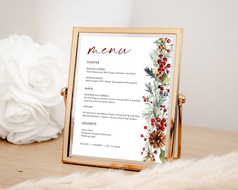 May include: A rectangular gold metal frame holding a printed menu card. The menu features the word menu in red script, followed by black text listing starters, mains, and desserts. A watercolor illustration of pine branches, red berries, and a pinecone.
