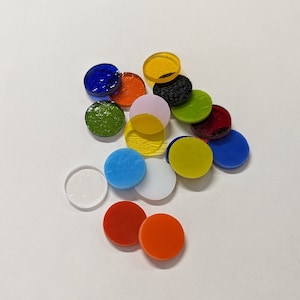 May include: Assortment of colorful round glass tiles in various shades of blue, green, yellow, red, orange, and white. The tiles are arranged in a random pattern on a white background.