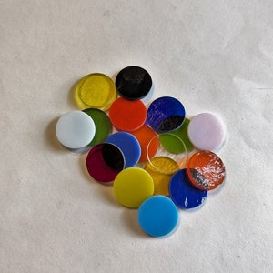 May include: A collection of colorful round glass pieces in various shades of red, blue, green, yellow, white, and black. The pieces are arranged in a cluster on a white surface.