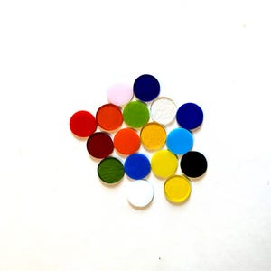 May include: A collection of colorful, round glass pieces in various shades, including red, orange, green, blue, and yellow. The pieces are arranged on a white surface, creating a visually appealing display of colors.