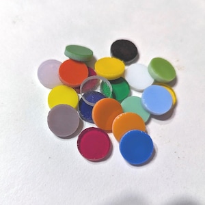 May include: A collection of small, flat, circular discs in a variety of solid colors including red, orange, yellow, green, blue, purple, white, and black. The discs have a smooth, opaque finish and are arranged in a loose, overlapping pile.