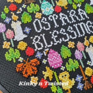 May include: Cross-stitch embroidery with a black background and colorful thread. The embroidery depicts a heart with the words "Love is a blessing" in white thread. The heart is surrounded by various colorful flowers, houses, butterflies, and other designs.