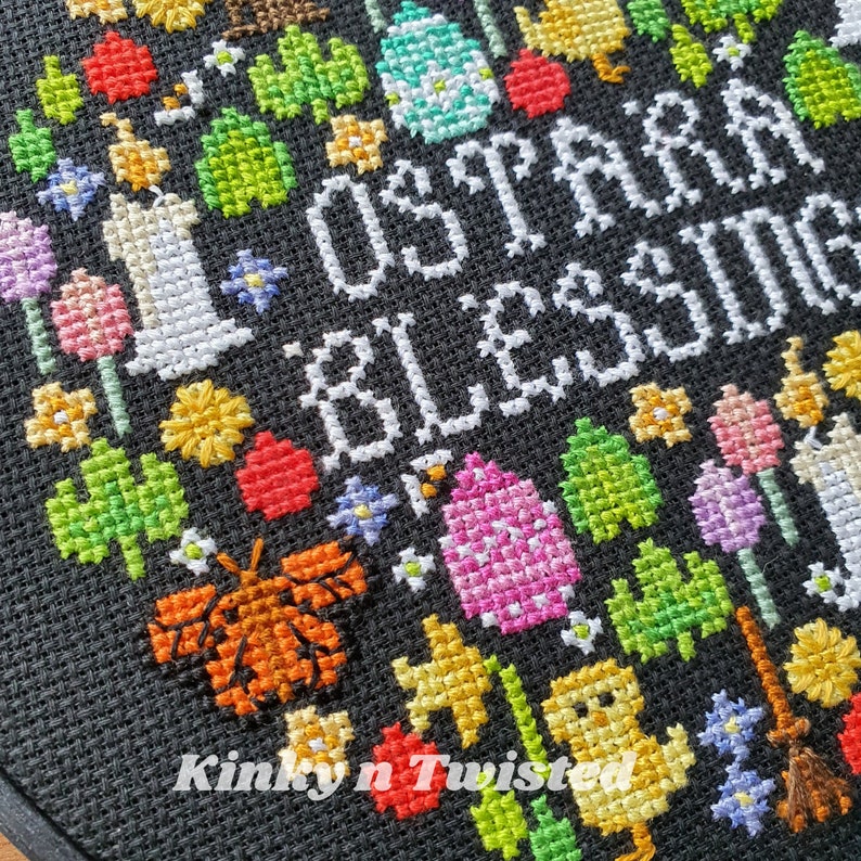 May include: Cross-stitch embroidery with a black background and colorful thread. The embroidery depicts a heart with the words "Love is a blessing" in white thread. The heart is surrounded by various colorful flowers, houses, butterflies, and other designs.