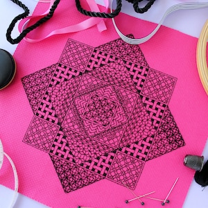 May include: A black and white geometric design embroidered on a bright pink fabric. The design is intricate and detailed, with a variety of shapes and patterns.