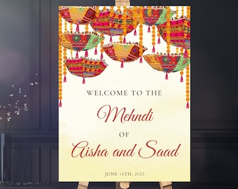 May include: A colorful welcome sign for a Mehndi celebration. The sign features a decorative border of hanging lanterns with intricate patterns and tassels. The text reads "Welcome to the Mehndi of Aisha and Saad June 14th, 2023".