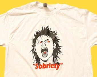 May include: White t-shirt with a black and white illustration of a person with red eyes and mouth, yelling with a pill in their mouth. The text "Sobriety" is printed in red below the illustration.