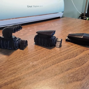 May include: Three black 3D printed engine models. The first model has a large intake manifold with multiple openings. The second model has a smaller intake manifold and a single opening. The third model is a single piece with a rounded shape.