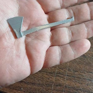 May include: A small, silver-colored axe with a wooden handle. The axe is about 5 inches long and is held in a person's hand.