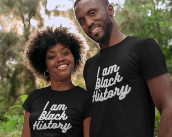 May include: A couple wearing black t-shirts with the text "I am Black History" in white lettering. The couple is standing in a forest setting.