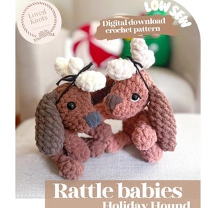 May include: Two brown and white crocheted rattle toys shaped like dogs with antlers. The toys are sitting on a light brown fabric surface. The text "Rattle babies Holiday Hound" is at the bottom of the image. The text "Low Sew Digital download crochet pattern" is at the top of the image.