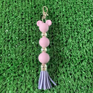 May include: A purple beaded keychain with a tassel. The keychain has a bear-shaped charm at the top.