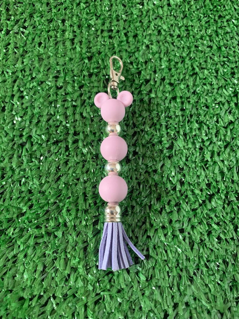 May include: A purple beaded keychain with a tassel. The keychain has a bear-shaped charm at the top.