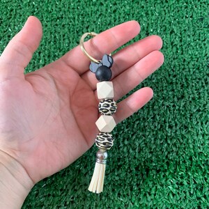 May include: A keychain with a black and white Minnie Mouse charm, a black bead, a white bead, a leopard print bead, a white bead, a silver bead, and a white tassel.