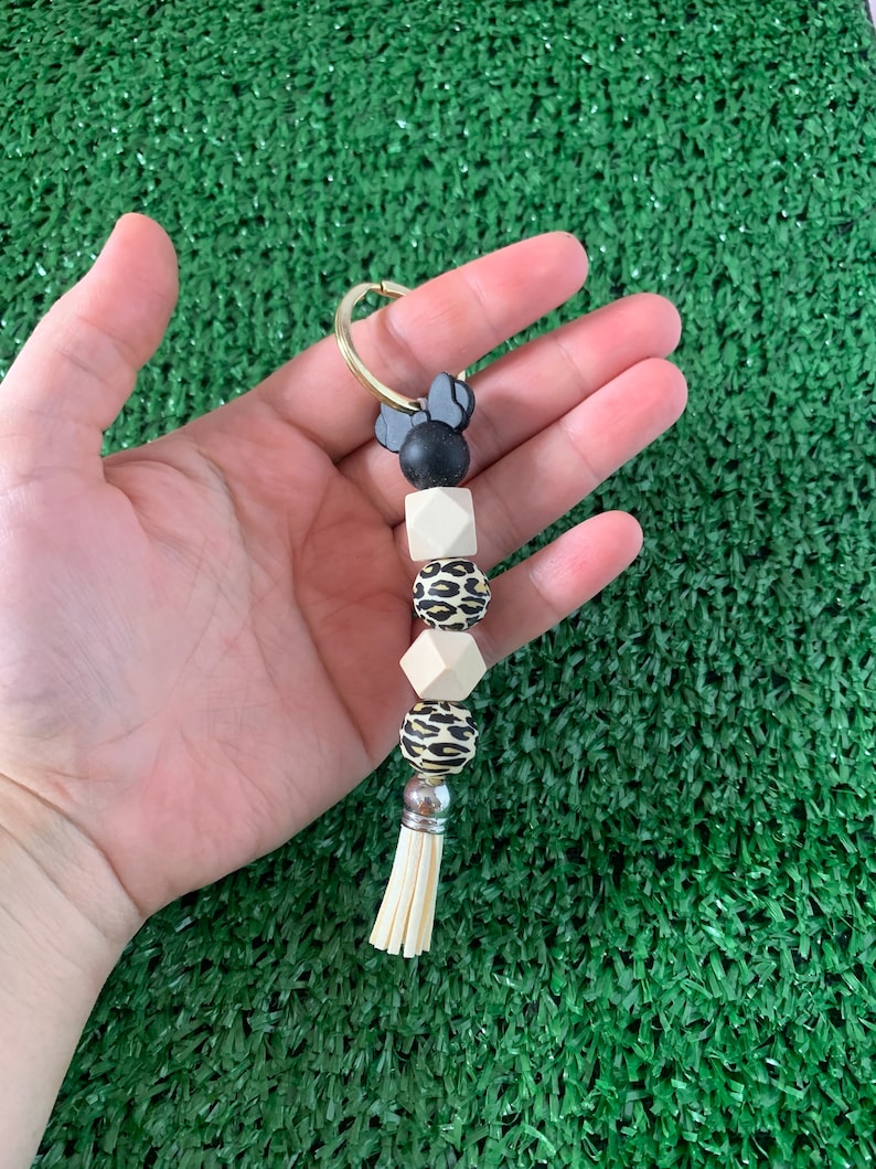 May include: A keychain with a black and white Minnie Mouse charm, a black bead, a white bead, a leopard print bead, a white bead, a silver bead, and a white tassel.