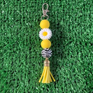 May include: A yellow and white beaded keychain with a daisy charm, zebra print bead, and a yellow tassel.
