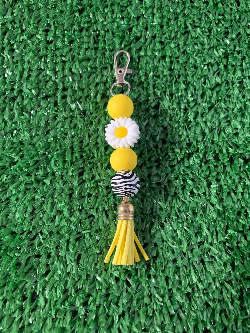 May include: A yellow and white beaded keychain with a daisy charm, zebra print bead, and a yellow tassel.