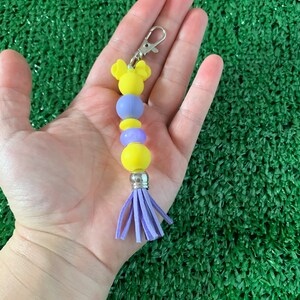 May include: A yellow and purple beaded keychain with a purple tassel and a Mickey Mouse head charm.