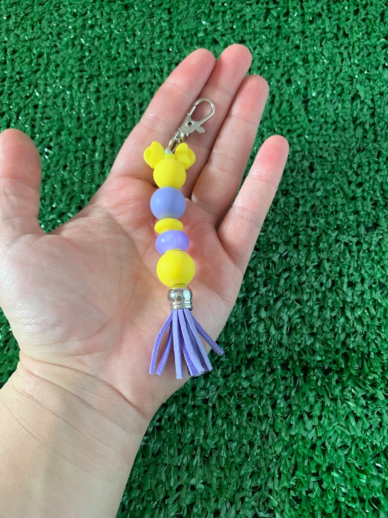 May include: A yellow and purple beaded keychain with a purple tassel and a Mickey Mouse head charm.