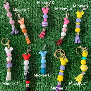 May include: Nine colorful beaded keychains with Mickey Mouse and Minnie Mouse character charms. The keychains feature different colors and patterns, including purple, pink, blue, yellow, and white.